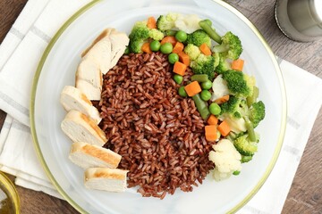 Delicious brown rice with chicken and vegetables served on wooden table, top view