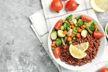 Delicious brown rice with vegetables and lemon slices served on grey textured table, flat lay. Space for text