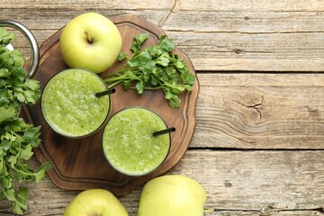 Healthy parsley smoothie in glasses, leaves and apples on wooden table, flat lay. Space for text