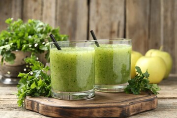 Healthy parsley smoothie in glasses and leaves on wooden table, closeup