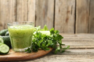 Healthy parsley smoothie in glass, leaves and cucumber on wooden table, closeup. Space for text