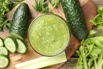 Healthy parsley smoothie in glass, leaves, cucumber and celery on wooden table, flat lay