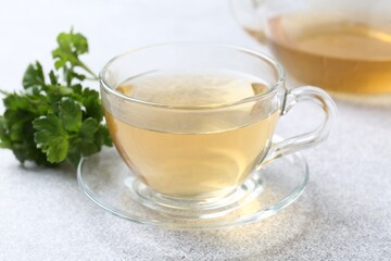 Aromatic herbal tea in glass cup and fresh parsley on light grey table, closeup