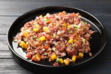 Tasty salad with brown rice on black wooden table, closeup