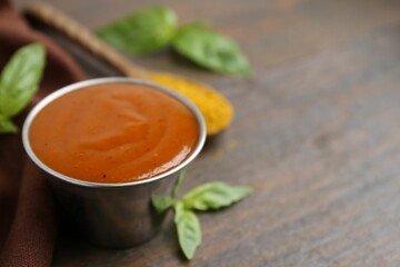 Tasty curry sauce in metal dish, powder and basil on wooden table, closeup. Space for text