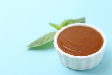Tasty curry sauce and basil leaves on light blue background, closeup. Space for text