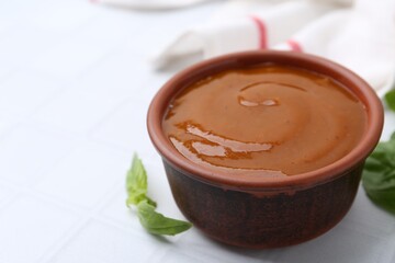 Tasty curry sauce and basil leaves on white tiled table, closeup. Space for text