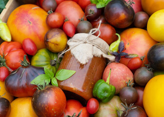 Wooden box with mix of multicolored ripe tomatoes stands on the garden bed. Fresh tomato, basil with a jar of ketchup for sale at the farmers market. Concept of gardening and delivery of organic food