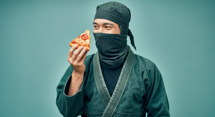 Asian male ninja holding pizza slice against teal background