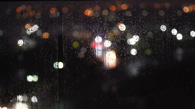 Horizontal video of defocused lights on the background and rain drops on the foreground at night.