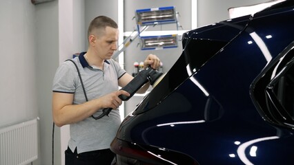 Car detailer uses a polisher to meticulously restore shine to a dark blue car's paintwork in a...