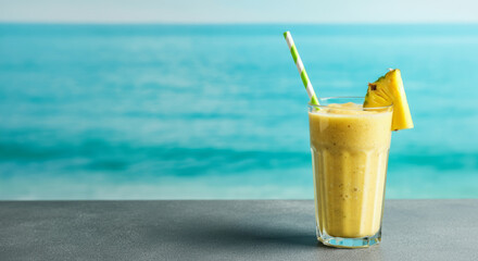 Tropical pineapple smoothie with paper straw by the ocean shoreline
