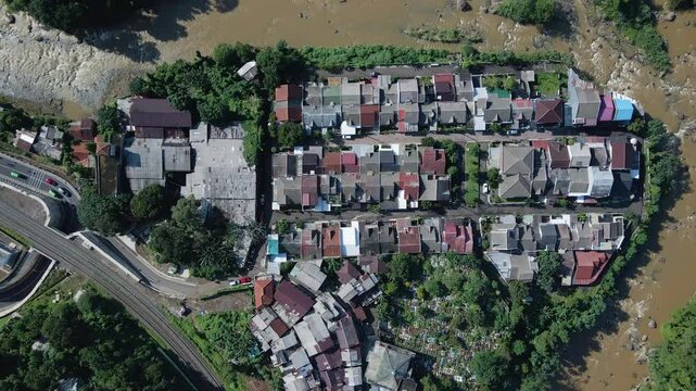 4K drone shot of a residential enclave wrapped by a curvy, muddy river amidst a lush tropical forest. The scene presents natural and human-made features coexisting in harmony and contrast