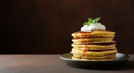 Stack of pancakes with syrup and cream topped with mint on dark background
