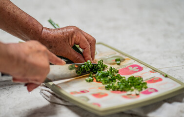 primer plano de mano de mujer mayor picando verduras en la cocina - foto de stock 