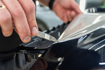 The process of installing PPF, armored film on the car. PPF is a polyurethane, protective film that protects the paint from scratches. Car wrapping, tuning, styling. Close-up, selective focus.