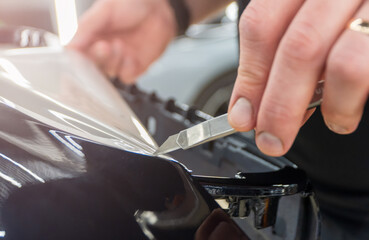 The process of installing PPF, armored film on the car. PPF is a polyurethane, protective film that protects the paint from scratches. Car wrapping, tuning, styling. Close-up, selective focus.