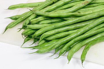 Green beans (Phaseolus vulgaris L) from a traditional market on a cutting board, white background.
