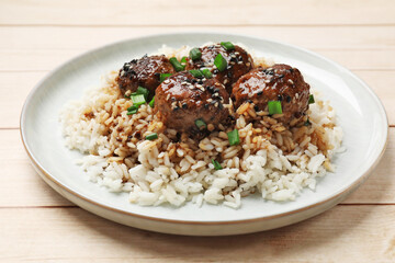 Delicious rice with meatballs, sauce and green onions on white wooden table, closeup