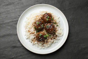Delicious rice with meatballs, sauce and green onions on black table, top view