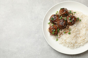 Delicious rice with meatballs, sauce and green onions on grey table, top view. Space for text