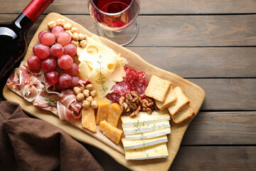 Different types of cut cheese and other snacks served with wine on wooden table, flat lay. Space for text