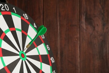 Dart board with arrow on wooden background, closeup. Space for text