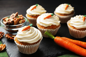 Tasty carrot muffins with cream, walnuts and fresh vegetables on black table, closeup