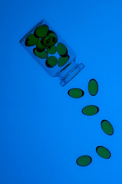 Green omega-3 and vitamin D capsules falling from jar