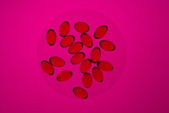 Red omega-3 and vitamin D capsules on a pink background