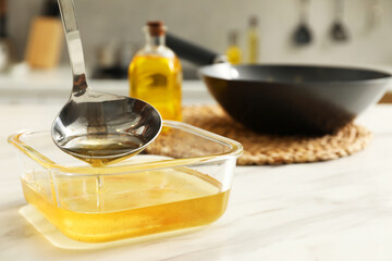 Pouring used cooking oil into glass container at white marble table, closeup