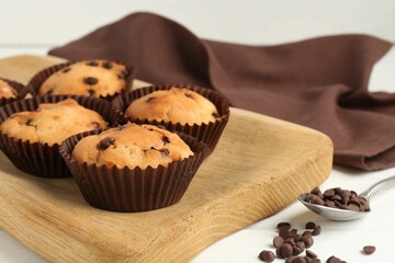 Delicious muffin with chocolate chips on white wooden table, closeup
