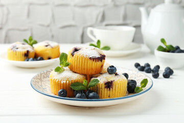 Delicious muffins with blueberries, powdered sugar and mint on white wooden table, closeup