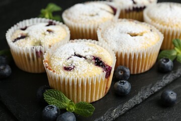 Delicious muffins with blueberries, powdered sugar and mint on dark textured table, closeup