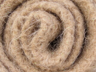 Closeup of rolled up beige wool scarf. Rolled up beige tricot texture.