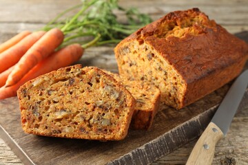 Homemade carrot cake with nuts, knife and vegetables on wooden table, closeup