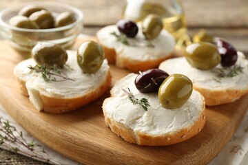 Delicious sandwiches with marinated olives, cream cheese and thyme on wooden table, closeup