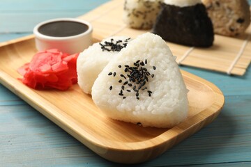 Rice balls (onigiri), soy sauce and pickled ginger on light blue wooden table, closeup. Traditional Japanese dish