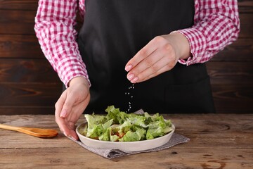 Woman salting tasty salad at wooden table, closeup