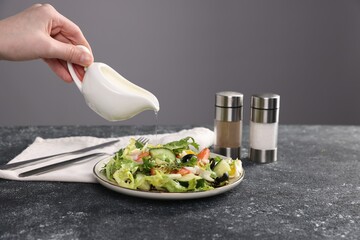 Woman pouring oil onto salad at dark textured table against grey background, closeup
