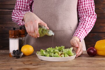 Woman pouring oil onto tasty salad at wooden table, closeup