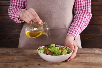 Woman pouring oil onto tasty salad at wooden table, closeup