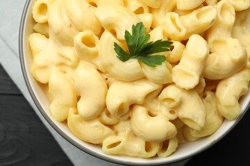 Delicious macaroni and cheese with parsley on black wooden table, top view