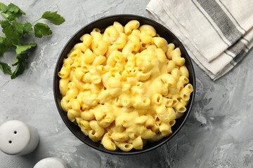 Delicious pasta with cheese sauce in bowl and parsley on grey table, flat lay