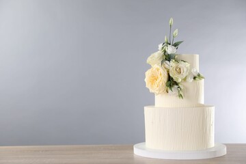 Delicious wedding cake decorated with flowers on wooden table against grey background. Space for text