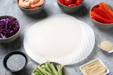 Rice paper sheets and different ingredients on light grey table, closeup