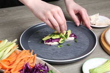 Woman making tasty spring roll at grey wooden table, closeup