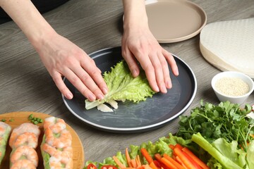 Woman making tasty spring roll at grey wooden table, closeup