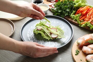 Woman making tasty spring roll at grey wooden table, closeup