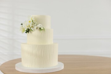 Delicious wedding cake with floral decor on wooden table indoors, space for text